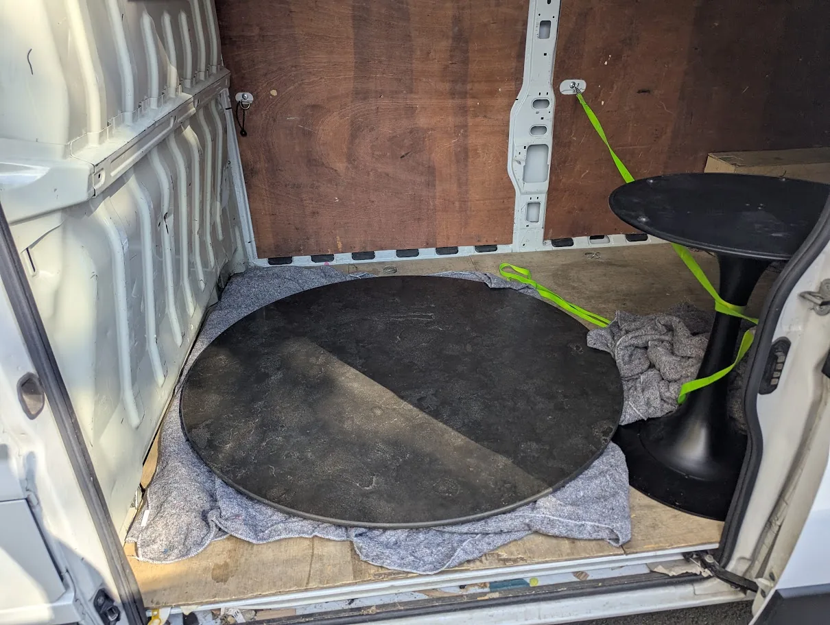 Heavy table components protected with blankets and straps inside the Arrow delivery van